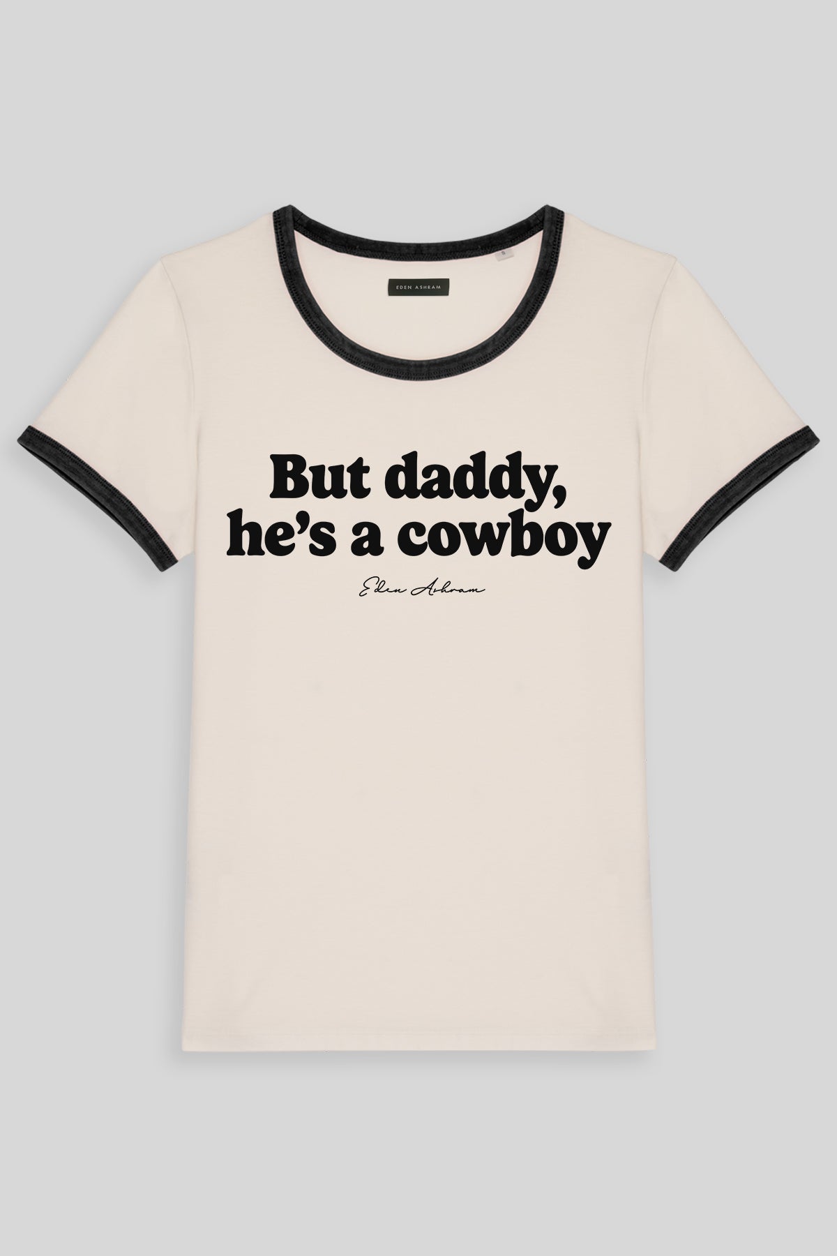 An organic cotton ringer t-shirt with black trim on the collar and sleeve cuffs, featuring the tprint 'But daddy, he's a cowboy'.
